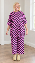 Front full view of model wearing magenta and black checkered tunic top and wide-leg crop pants set