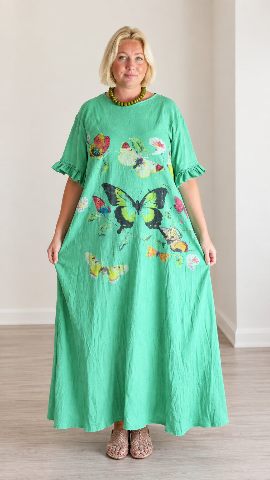 Front view of woman wearing a loose green butterfly print maxi dress with ruffle sleeves