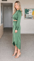Side angle view of model wearing sage green satin long sleeve crop top and midi skirt