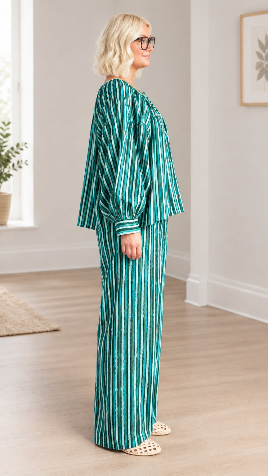 Side profile view of model in green striped balloon-sleeve top and matching wide-leg trousers