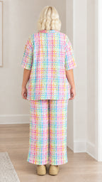 Back view of model in pastel plaid plissé button-up shirt and wide-leg trousers