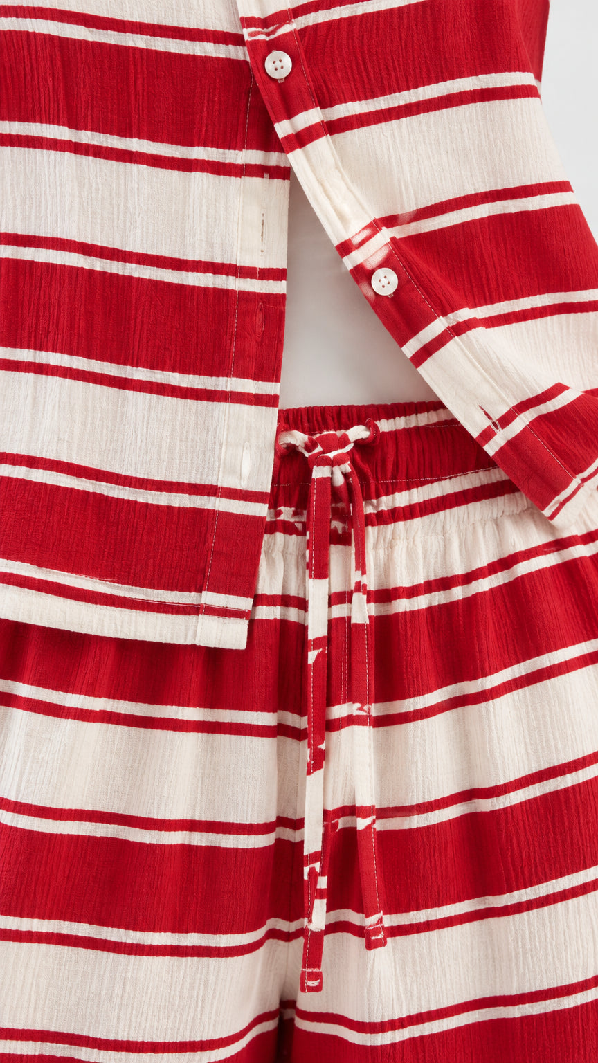 Close-up detail of button closure, fabric texture, and drawstring waistband on red and white striped set