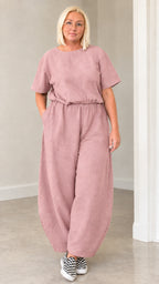 Front view of woman wearing dusty pink short sleeve lantern jumpsuit